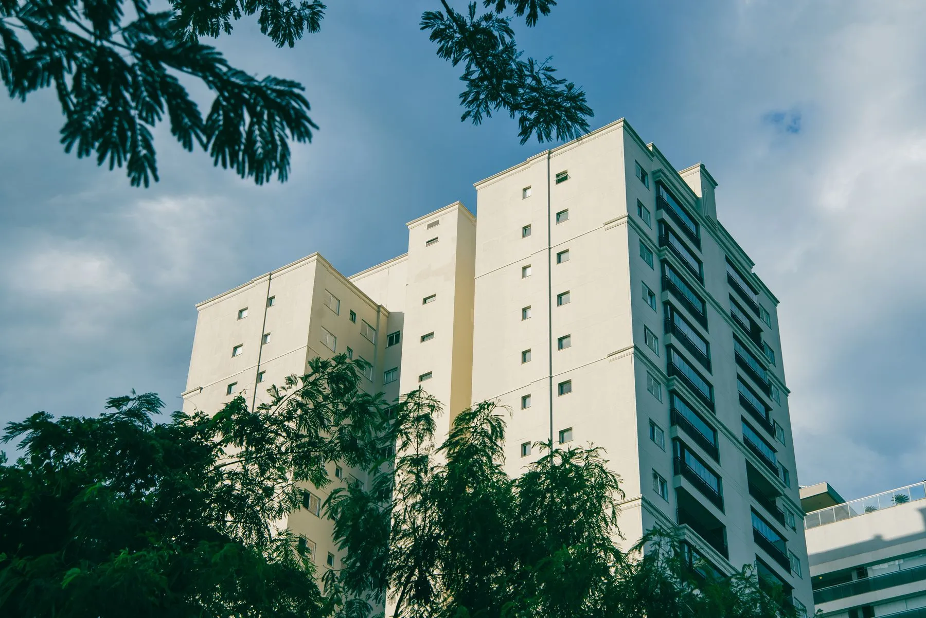 Prédio residencial alto entre árvores, sob céu azul